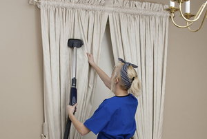 woman cleaning light-colored drapes