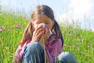 A little girl sitting in a grassy field and blowing her nose because she has a grass allergy.