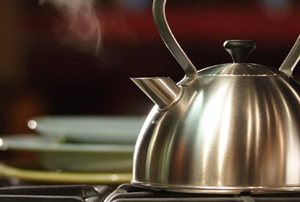 A steaming, stainless steel tea kettle.
