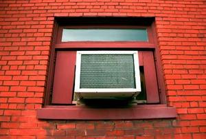 A small air conditioner in the window of a brick apartment building.