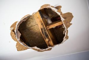 A hole in a ceiling exposing pipes and beams.