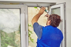 person applying caulk to the inside of a window frame
