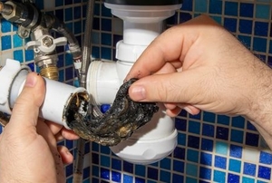 hands removing hair clog from corrugated drain pipe under bathroom sink