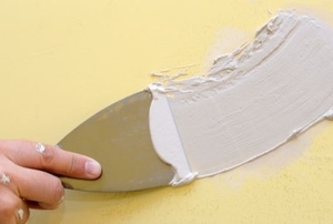putty knife applying spackle to patch a yellow wall