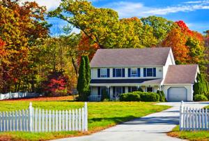 A white, two-story house against a backdrop of colorful, fall leaves.