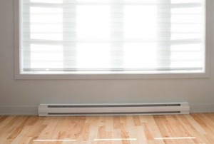 A white baseboard heater in a room with a hardwood floor.
