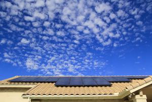 A roof with solar panels on it against a blue cloudy sky.