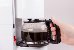 A person pulling a full pot of coffee from the coffeemaker.