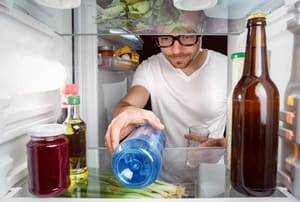 Man moving a bottle inside a refrigerator.
