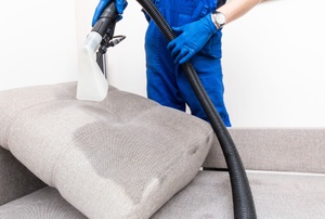 A man using a handheld steam cleaner on a cushion