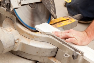 A construction worker cutting a board at an angle on a miter saw.