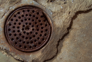A rusty old basement drain in a concrete floor.