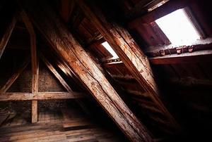 A corner of a darkly-lit, old attic with a small window on the wall.