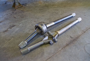 The front drive axle to a truck lying on the ground in a garage.