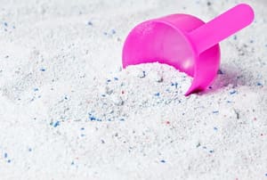 A pile of laundry detergent with a pink scoop. 
