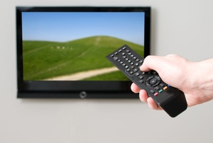 person pushing button on remote aimed at TV on the wall