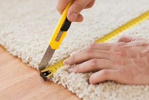 hands measuring and cutting a carpet with a tape measure and construction knife