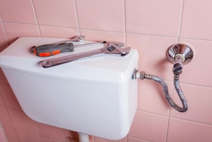 A toilet tank with tools on top and a pink tile wall.