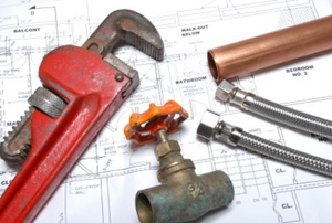 A copper pipe, wrench, valve, and bolts sit on top of construction plans.