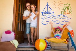 A family of three at a summer vacation house with pool toys and an ocean scene on the wall.