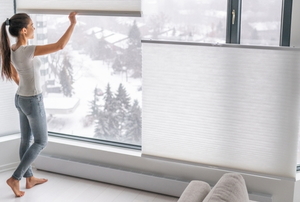 woman opening pleated blinds in front of snowy town