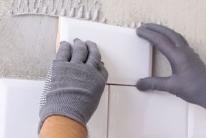 gloved hands mounting white tiles to wall