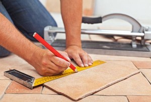 A diy-er measuring tile with a ruler and pencil.