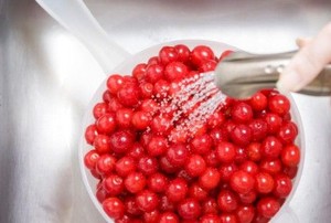 a hand holds a kitchen faucet hose over cranberries, rinsing them