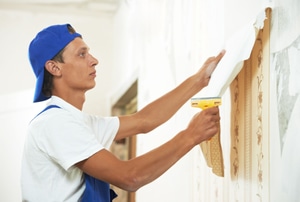 A handyman stripping a wall of wallpaper. 