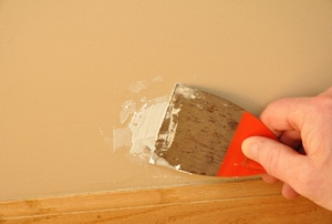 A man uses spackling compound on a wall