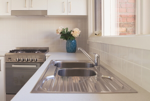 A stainless steel sink and oven in a white kitchen with flowers in a blue vase. 