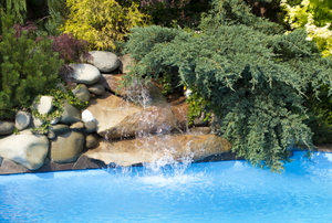 Water flows from a rock waterfall at the side of a swimming pool.