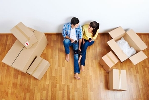 A couple sitting on the ground, surrounded by moving boxes.