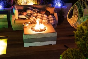 a person sleeping outdoors under blanket near propane firepit