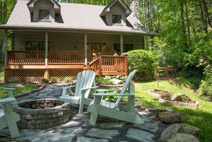 A cabin home with adirondack chairs around a fire pit.