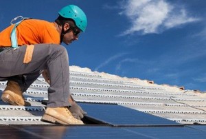A worker lays solar panels on top of a roof.