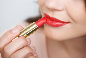 A woman applying glossy red lipstick to her lips.