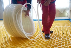 workers laying radiant floor heating tubes on yellow pegged mat