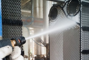 gloved hands power washing a plate heat exchanger