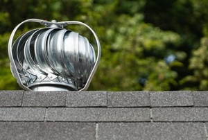 attic fan on roof in front of leaves