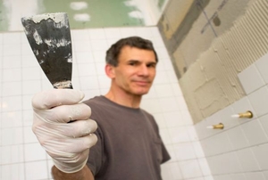 Man in a bathroom holding up a scraper.
