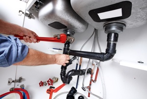 A man adjusts pipes under a sink.