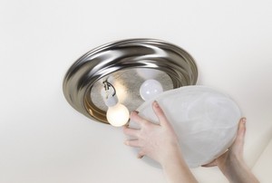 A woman installs a light fixture.