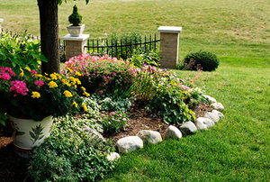 Garden patch bordered by large stones with decorative fence in background.