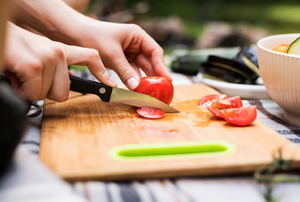 A woman cuts a tomato on a cutting board.