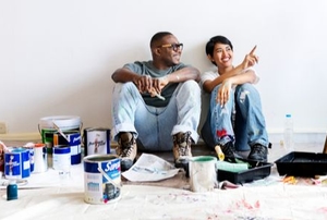 two smiling people in an apartment room with painting supplies looking at the walls