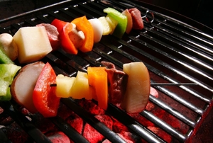 Skewers cooking on a stainless steel grill grate.