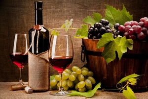 Two wine glasses and a bottle of red wine sit beside a bucket of grapes.