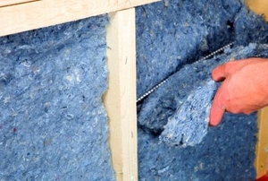 Installing recycled blue jean denim insulation between wall studs.