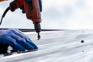 hands with drill installing metal roof